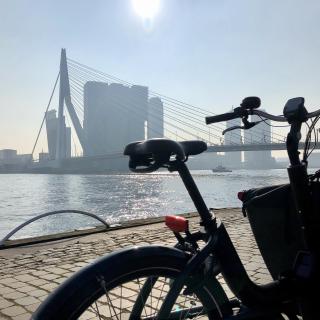 zwarte bakfiets geparkeerd op de kade met op de achtergrond de Erasmusbrug