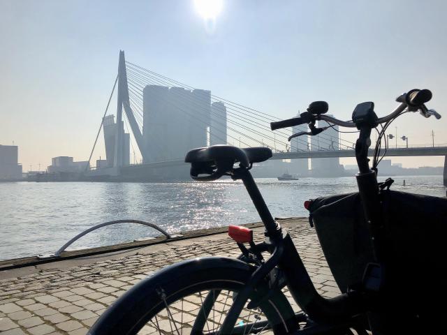 zwarte bakfiets geparkeerd op de kade met op de achtergrond de Erasmusbrug