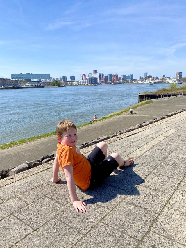 jongen langs een rivier met in de verte de skyline van rotterdam