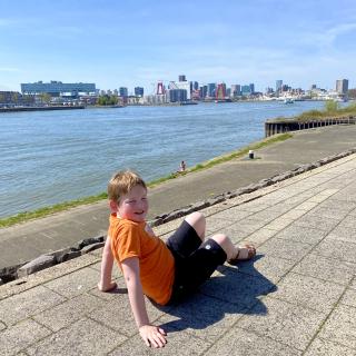 jongen langs een rivier met in de verte de skyline van rotterdam