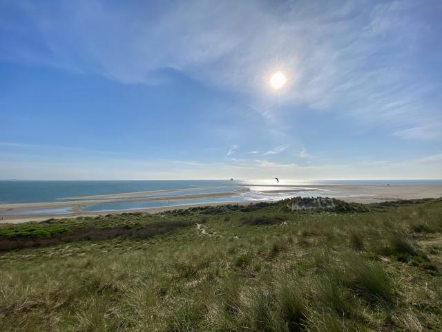 duinen en strand met in de verte een ondergaande zon boven de zee