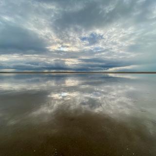 de lucht weerspiegelt in een laagje water op het strand