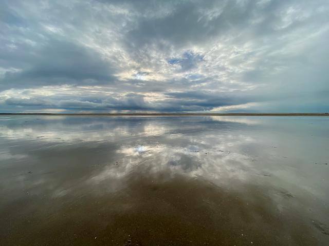 de lucht weerspiegelt in een laagje water op het strand