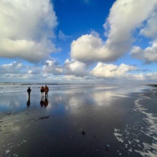 personen in de branding van de zee, met een half bewolkte lucht weerspiegeld in een laagje water