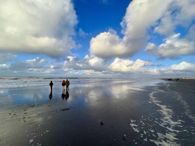personen in de branding van de zee, met een half bewolkte lucht weerspiegeld in een laagje water