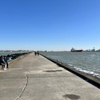 de pier van Hoek van Holland richting kust, met links het strand en rechts de Nieuwe Waterweg met een groot vrachtschip
