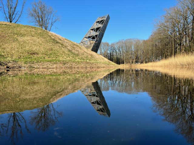 een schuin oplopende houten toren, weerspiegeld in het water