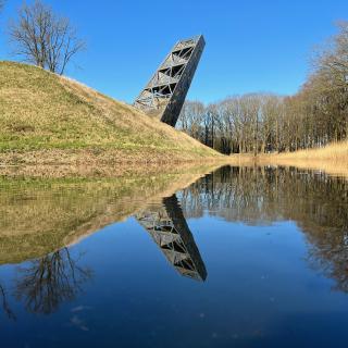 een schuin oplopende houten toren, weerspiegeld in het water