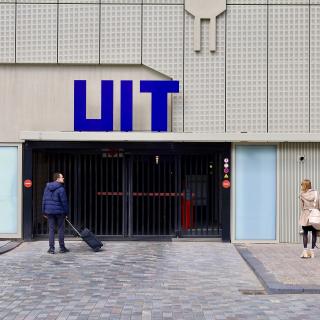 Twee mensen bij een gesloten ingang met blauwe letters UIT op een gebouw.