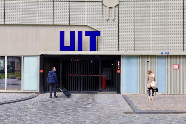 Twee mensen bij een gesloten ingang met blauwe letters UIT op een gebouw.