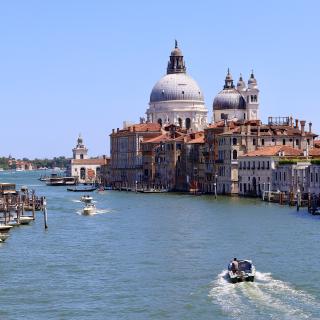 Een boot vaart over een kanaal in Venetië met de Basilica di Santa Maria della Salute op de achtergrond onder een blauwe hemel.