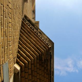 Bruine bakstenen muur met een zigzagpatroon onder een blauwe lucht met wat wolken.