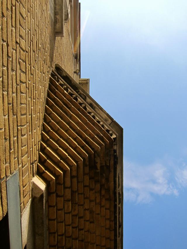 Bruine bakstenen muur met een zigzagpatroon onder een blauwe lucht met wat wolken.