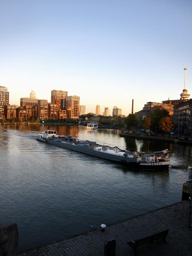 Een grote boot vaart over een rivier langs moderne gebouwen bij zonsondergang.