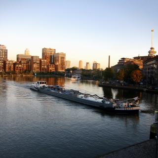Een grote boot vaart over een rivier langs moderne gebouwen bij zonsondergang.