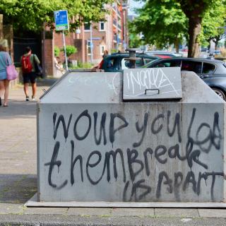 Graffiti op een afvalcontainer in een straat.