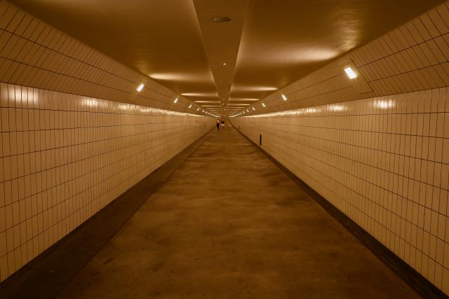 Lange, goed verlichte tunnel met witte tegelwanden en een betonnen vloer, met een paar mensen in de verte.