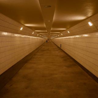 Lange, goed verlichte tunnel met witte tegelwanden en een betonnen vloer, met een paar mensen in de verte.