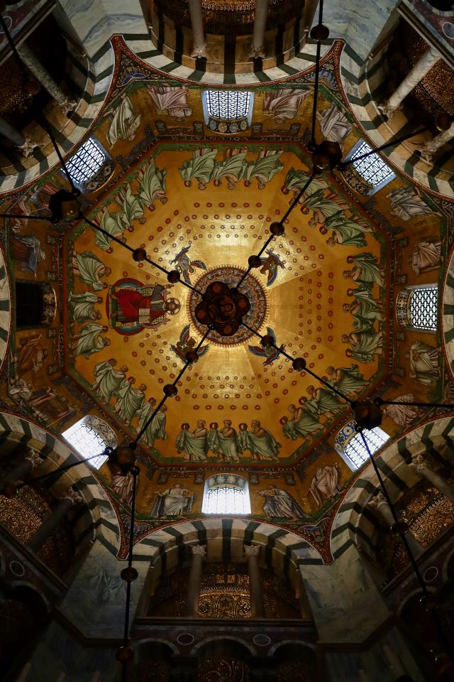 Gouden koepel met religieuze mozaíeken en engelen, omgeven door ramen en decoratieve bogen in een historische kerk.