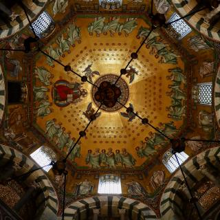 Gouden koepel met religieuze mozaíeken en engelen, omgeven door ramen en decoratieve bogen in een historische kerk.